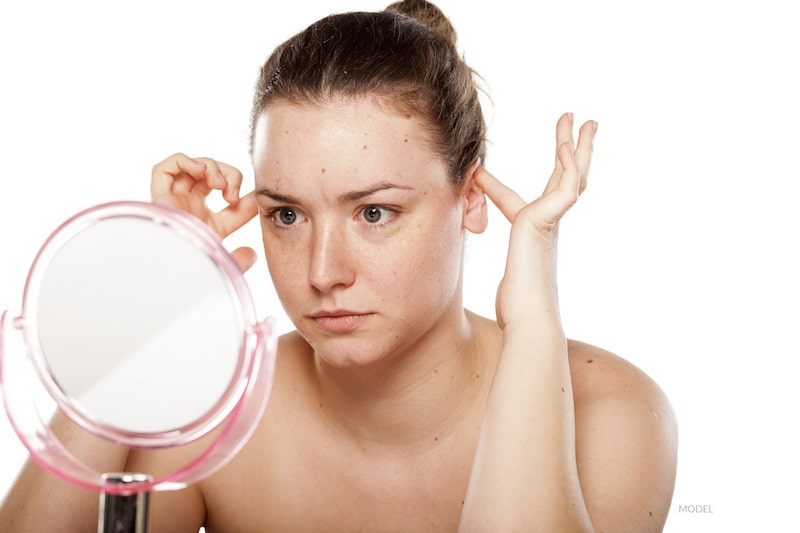 Woman looking at her reflection in the mirror while pushing her ears in and up on her head