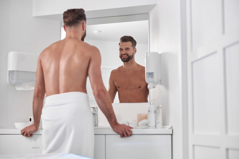 Attractive man in a towel, smiling at his reflection in the mirror