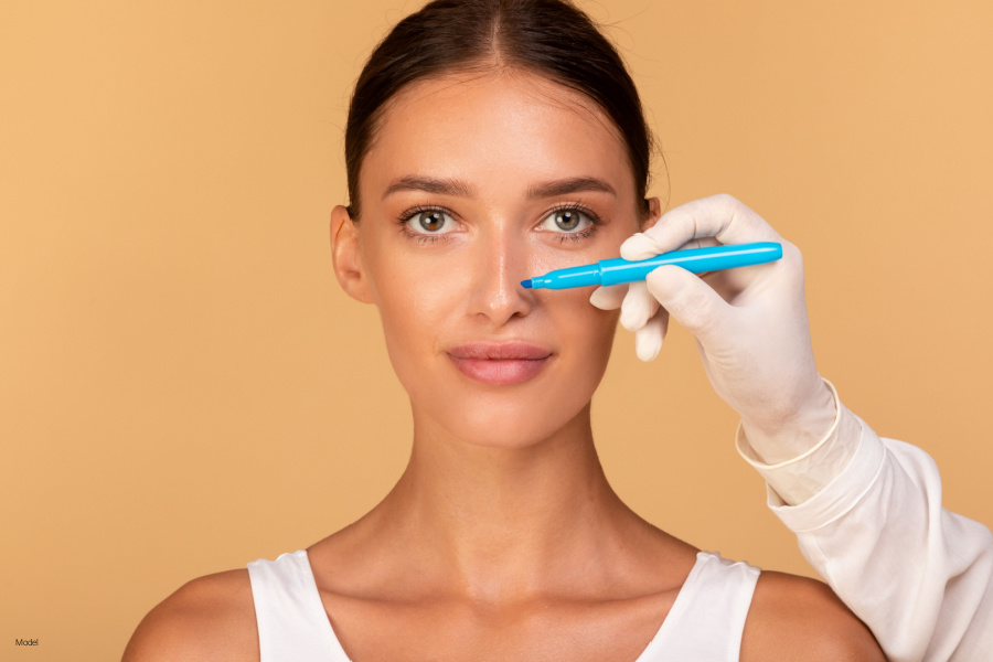 A woman looks at camera while a medical worker holds a blue marker beside her nose. 